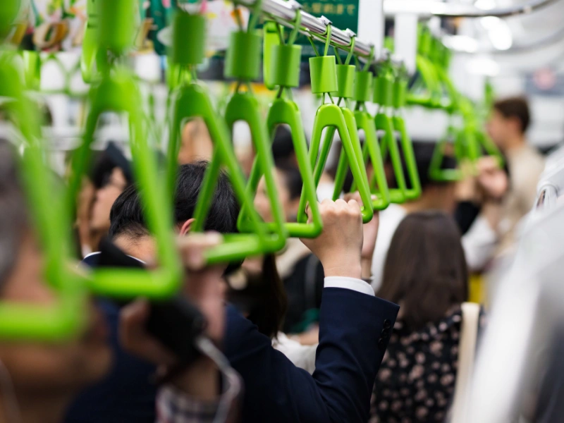 Crowded Japanese public transport with passengers standing and holding green hand straps, reflecting the quiet and orderly atmosphere typical of trains in Japan.