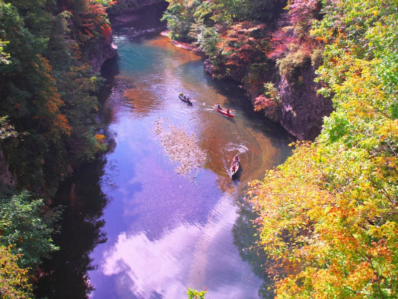 Scenic river at Jozankei Onsen with autumn foliage and boats paddling through calm waters.