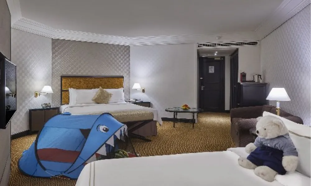 Spacious family-friendly hotel room at Grand Millennium Kuala Lumpur featuring a king bed, sofa, kids’ play tent, and plush teddy bear for a cozy stay.