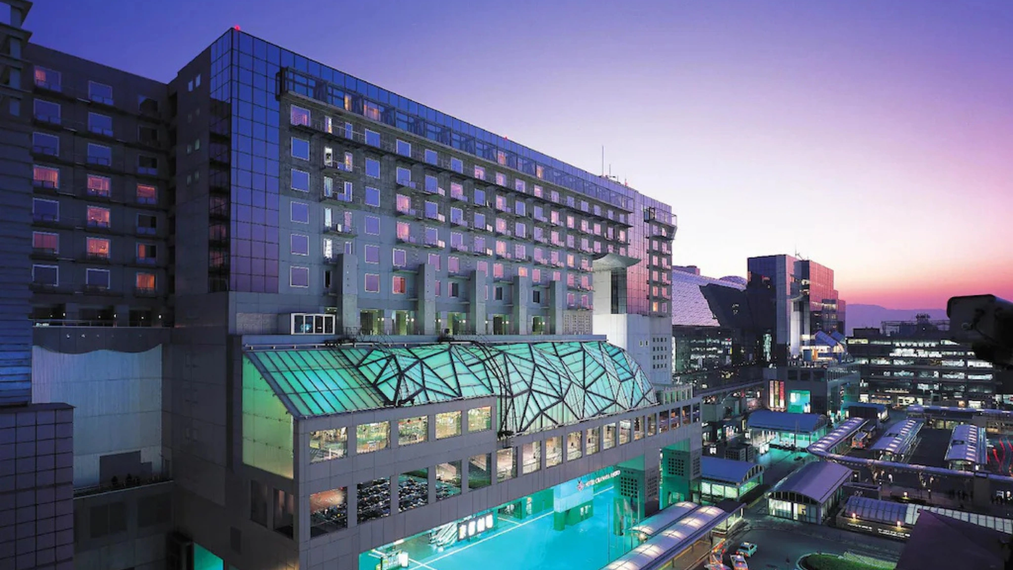 The modern, expansive architectural exterior of Hotel Granvia Kyoto during a purple sunset.