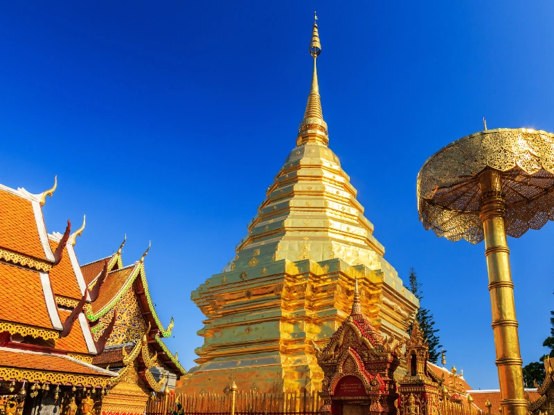vGolden Buddhist temple with a large central stupa and ornate architectural details under a clear blue sky, featuring a gGolden Buddhist temple with a large central stupa and ornate architectural details under a clear blue sky, featuring a golden umbrella-like structure on the right.olden umbrella-like structure on the right.