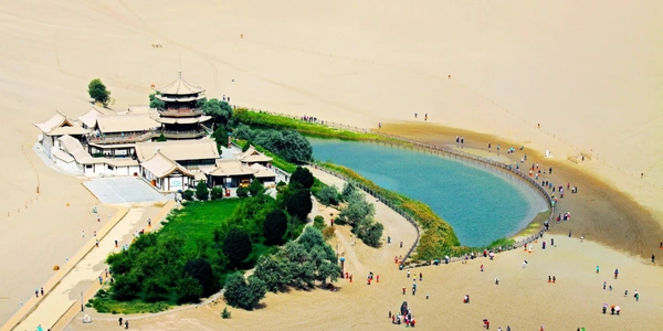 Crescent Lake Oasis in Dunhuang, China, surrounded by vast Gobi Desert sand dunes and traditional Chinese architecture, a famous eco-tourism and Silk Road travel destination.