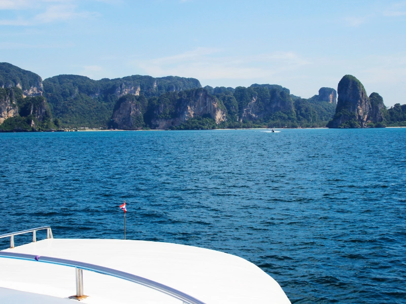 View from a boat deck overlooking the ocean, with lush green cliffs and rock formations under a clear blue sky.