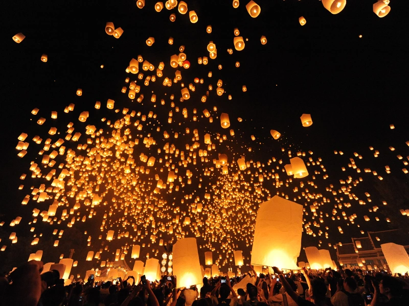 A night sky filled with glowing paper lanterns released by a crowd of people, creating a mesmerizing display.