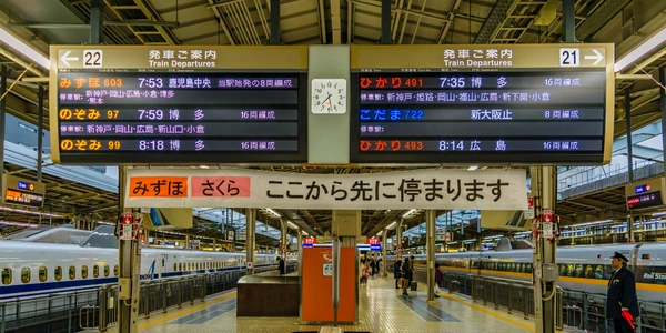 Osaka train station platform with Shinkansen trains and digital departure boards.