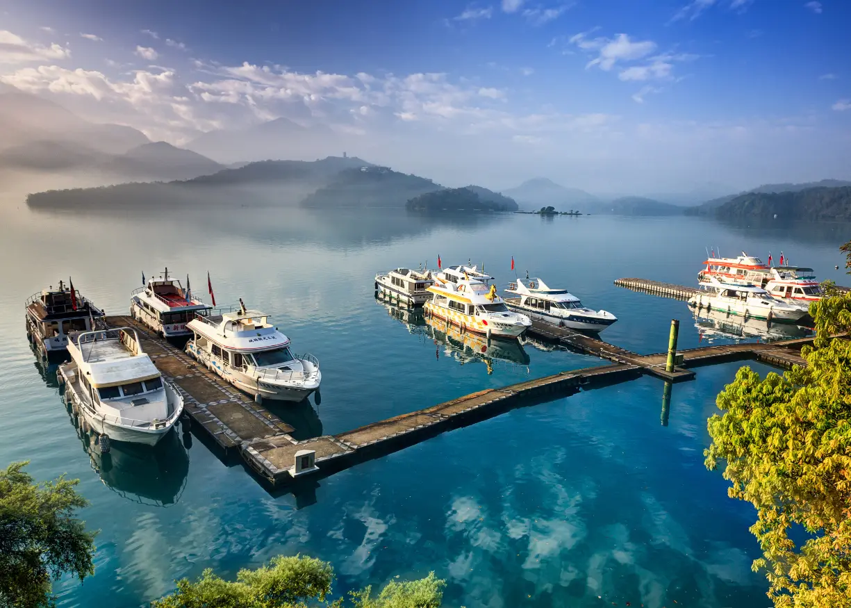 Tour boat cruising across the calm, turquoise waters of Sun Moon Lake in Taiwan, surrounded by lush mountains and scenic piers like Shuishe, Xuanguang Temple, and Ita Thao. A popular destination for nature lovers and cultural explorers, offering panoramic lake views and peaceful rides.