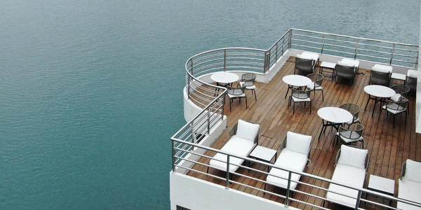 An upper wooden deck of a houseboat at Tasik Kenyir featuring white lounge chairs and round dining tables overlooking the lake