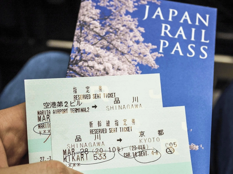 Japan Rail Pass booklet with cherry blossoms on the cover, alongside two reserved seat tickets for the Hikari 533 train from Narita Airport Terminal 2 to Shinagawa and from Shinagawa to Kyoto, both dated March 28 at 22:10.