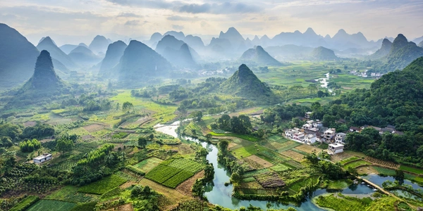 Karst mountains and lush countryside in Guilin, Guangxi, China, featuring winding rivers, green farmlands, and dramatic limestone peaks in one of the country's most scenic eco-tourism destinations.