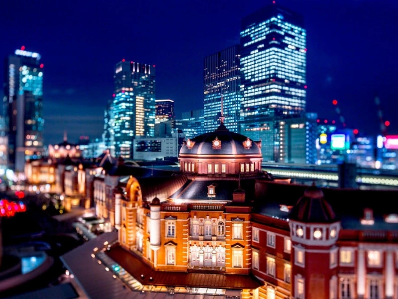 Tokyo Station Hotel at night with its historic facade lit up, framed by modern skyscrapers.