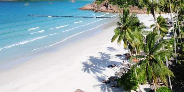 Top view of a wide white sand beach with palm trees and turquoise ocean waves at Long Beach Redang Island