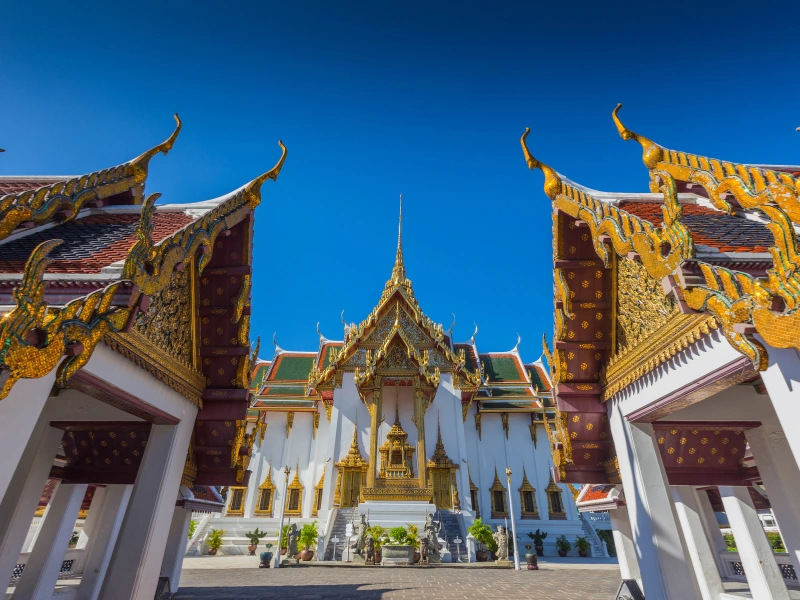 Ornate architecture of the Grand Palace in Bangkok, Thailand, featuring golden spires and detailed carvings under a clear blue sky
