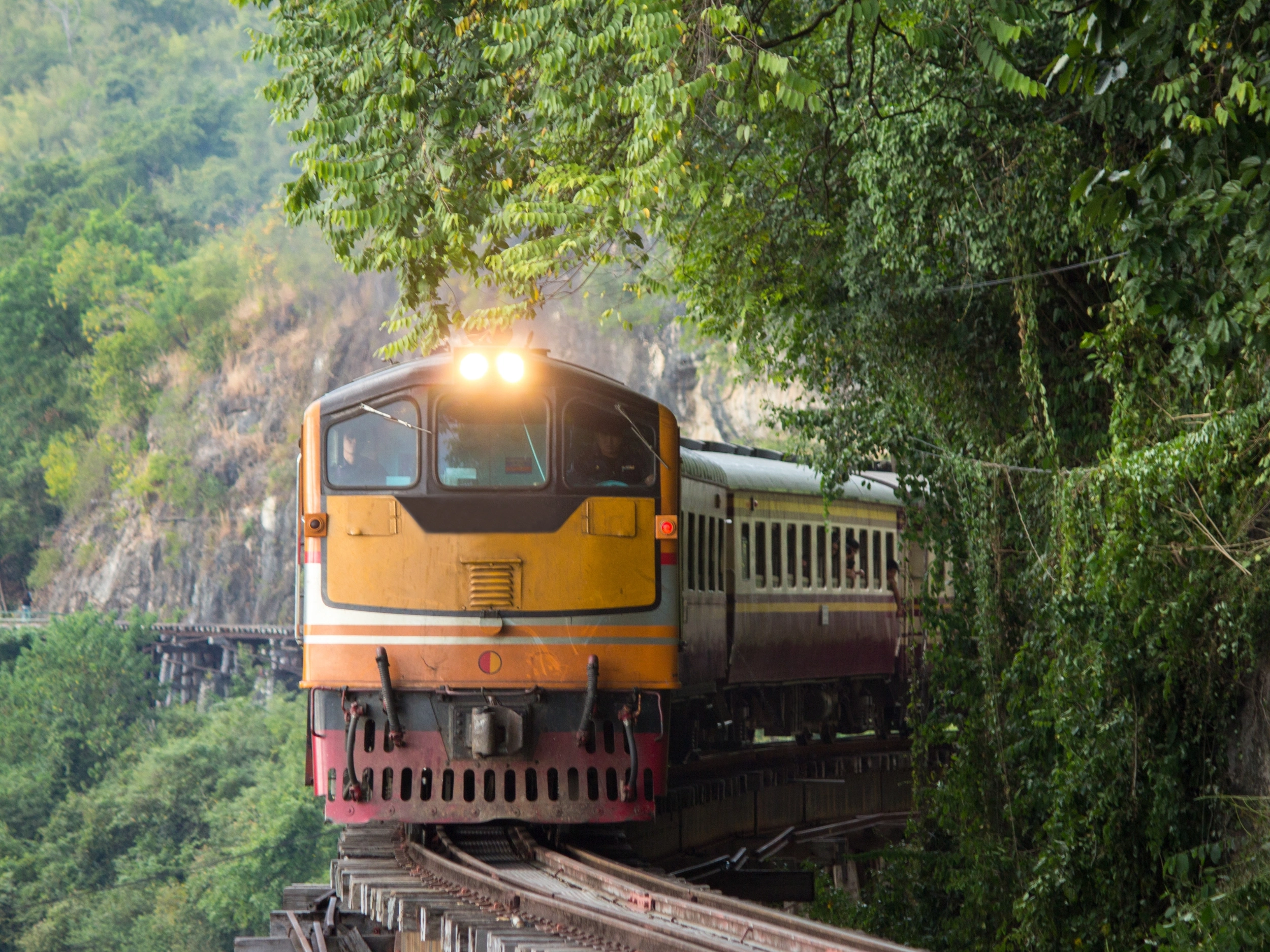 A train traveling on a railway track along the edge of a cliff. The cliffside is rugged and steep, with a scenic view of the landscape below. The train is visible from the side, with several carriages following the locomotive.